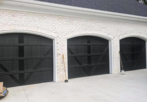 Three newly installed black carriage-style garage doors on a white brick home by Next Level Garage Doors in Locust Grove, GA.