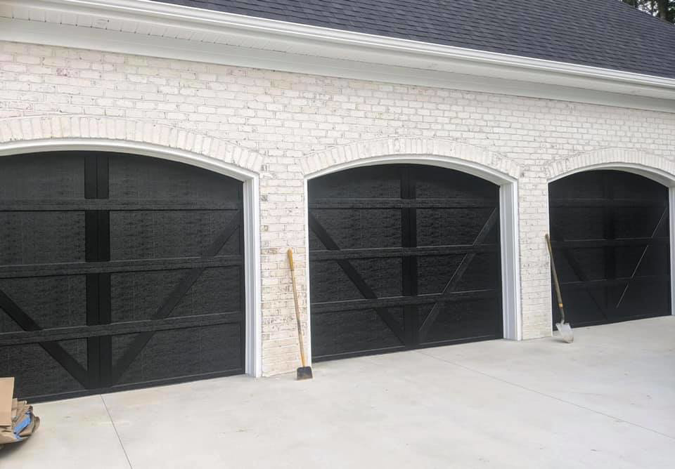 Three newly installed black carriage-style garage doors on a white brick home by Next Level Garage Doors in Locust Grove, GA.