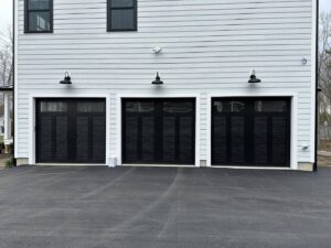 Three modern black garage doors with top windows on a light-colored house, installed by Steve Shumsky Unlimited Overhead Doors LLC in Hudson, NH