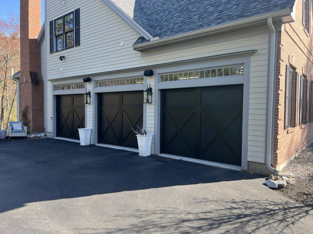 Three black garage doors with decorative windows installed on a residential home by NDI Garage Door in Plaistow, NH.