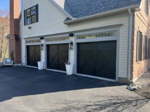 Three black garage doors with decorative windows installed on a residential home by NDI Garage Door in Plaistow, NH.