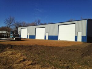 Three white commercial garage doors installed on a blue and grey metal building by Alberts Custom Door Company in Wichita, KS.