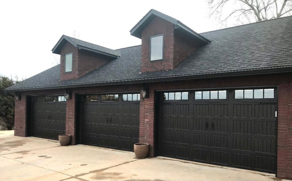Three dark brown residential garage doors installed on a brick house by Overhead Door Company of Mid-Ohio Valley in Parkersburg, WV.