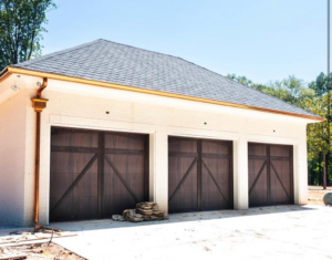 A garage building showcasing three dark wood-look garage doors with X-bracing installed by Bailey Garage Doors MT in Belgrade, MT.