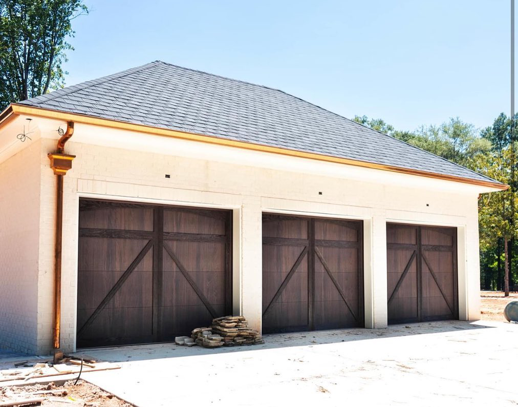 A garage building showcasing three dark wood-look garage doors with X-bracing installed by Bailey Garage Doors MT in Belgrade, MT.