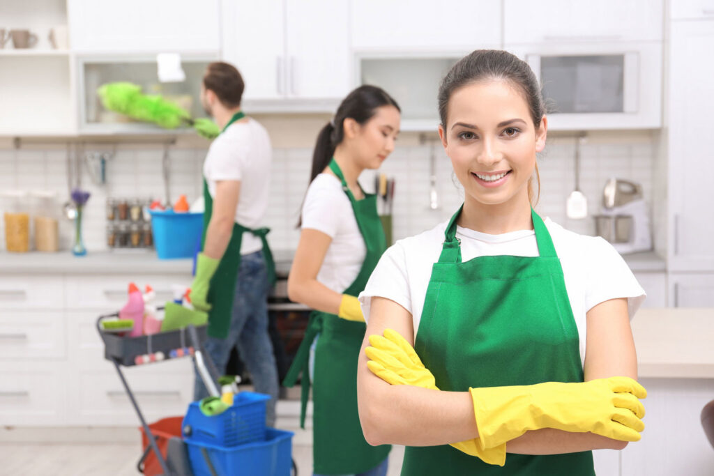 Three professional house cleaners from Northwest Cleaners tidying a kitchen in Portland, OR, with one dusting a shelf.