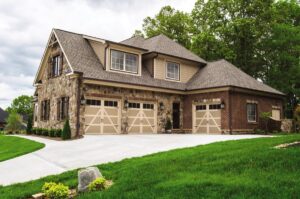 Three light-colored X-brace style garage doors on a stone and brick home by Access Door Systems in Uniontown, PA.