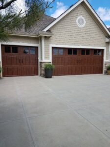 A residential property featuring three modern brown garage doors with stone accents, installed by JLM Garage Doors Omaha in Papillion, NE.