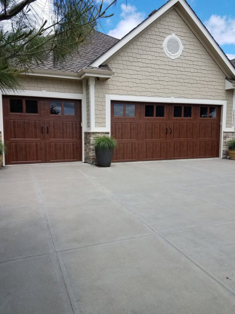 A residential property featuring three modern brown garage doors with stone accents, installed by JLM Garage Doors Omaha in Papillion, NE.