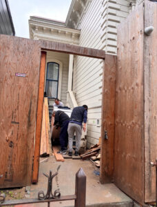 Three movers carrying a large, wrapped appliance through a narrow outdoor passage for IMoving Professional Moving System Inc. in San Francisco, CA