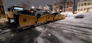 Three pickup trucks equipped with snow plows parked on a snowy street at night by TPM Snow Removal in Schenectady, NY.