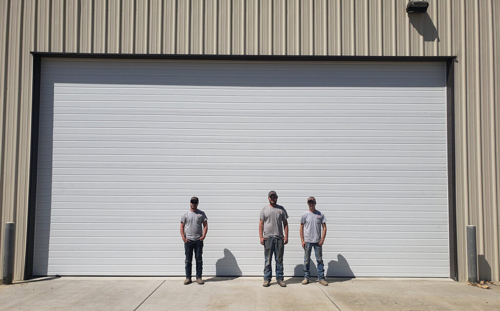 Three technicians standing in front of a large white commercial garage door, likely after installation or service by Overhead Door Company of Nampa in Nampa, ID.