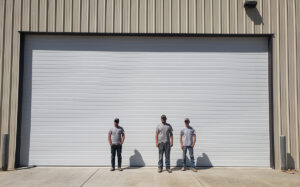 Three technicians standing in front of a large white commercial garage door, likely after installation or service by Overhead Door Company of Nampa in Nampa, ID.