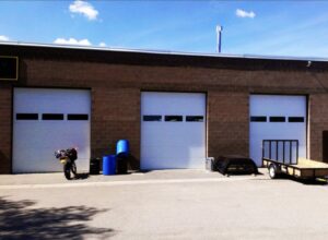 Three white commercial-style garage doors on a brick building, installed by Mark's Garage Door Services in Santa Fe, NM.