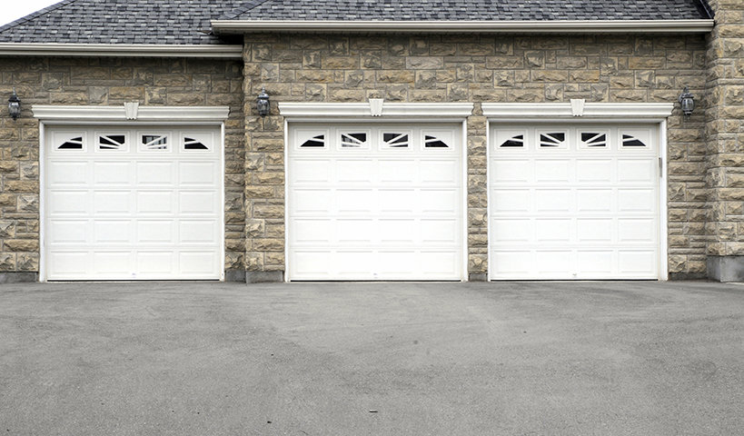 Three white garage doors with decorative windows installed on a stone house by K & B Door Co. in Las Vegas, NV