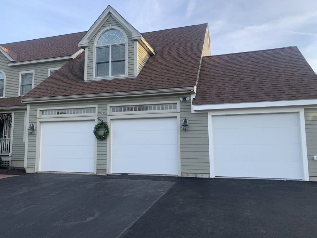 Three white garage doors with top windows installed on a residential home by J.A. Overhead Door in Westfield, MA.