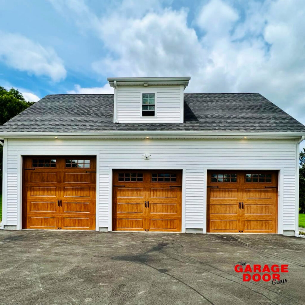 Three newly installed wooden-look garage doors with windows by The Garage Door Guys, LLC in New Haven, CT.