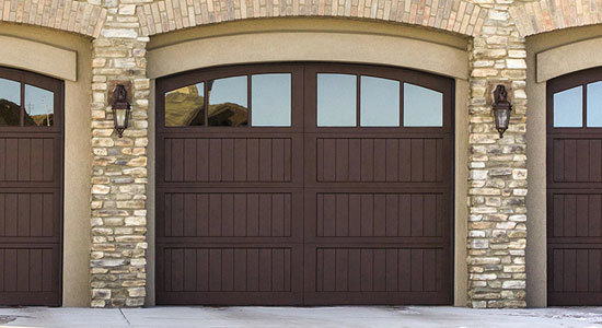 Three wooden-style garage doors with windows on a modern home by Custom Overhead Doors of Southern New Mexico in Alamogordo, NM.
