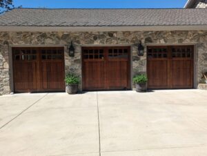 Three elegant wooden-style residential garage doors installed on a stone house by Canyon Overhead Doors in Salt Lake City, UT.