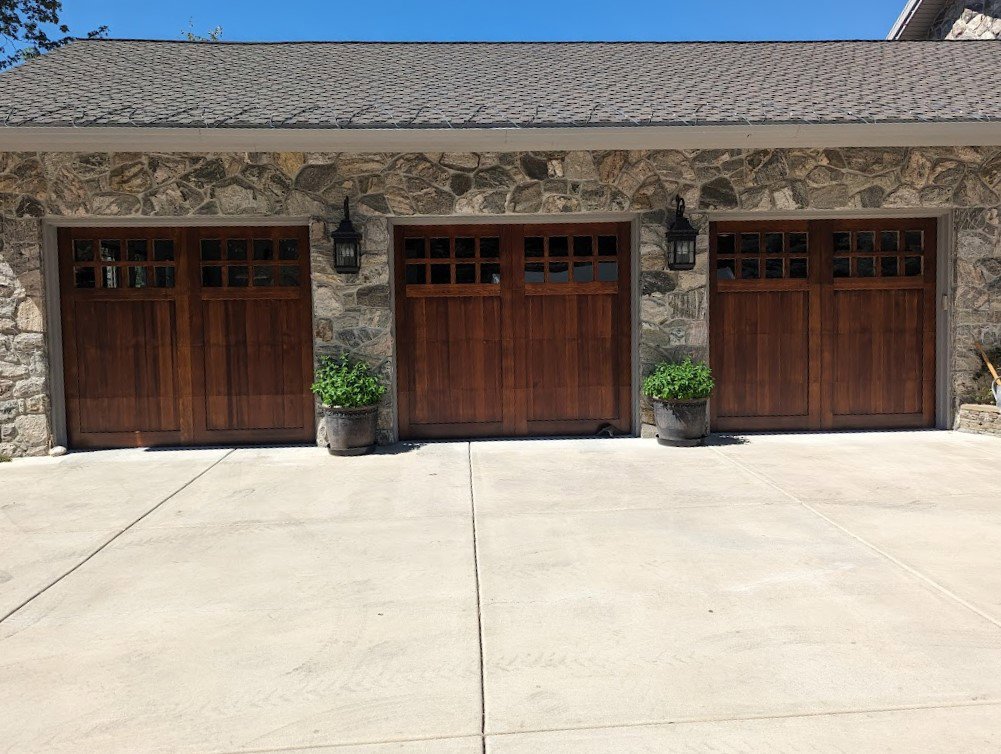 Three elegant wooden-style residential garage doors installed on a stone house by Canyon Overhead Doors in Salt Lake City, UT.