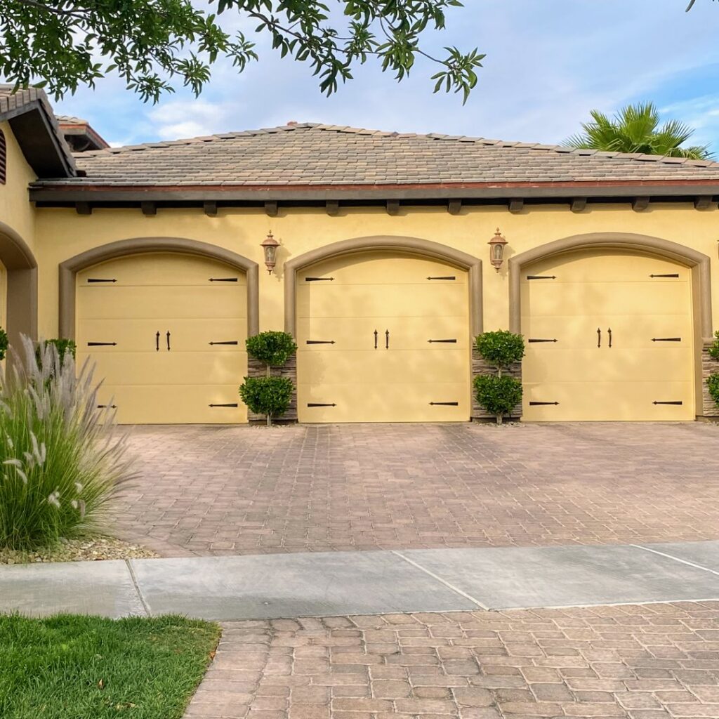 Three elegant yellow carriage-style garage doors with decorative hardware on a residential home, installed by American Veteran Garage Door Repair Henderson, NV.