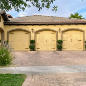 Three elegant yellow carriage-style garage doors with decorative hardware on a residential home, installed by American Veteran Garage Door Repair Henderson, NV.