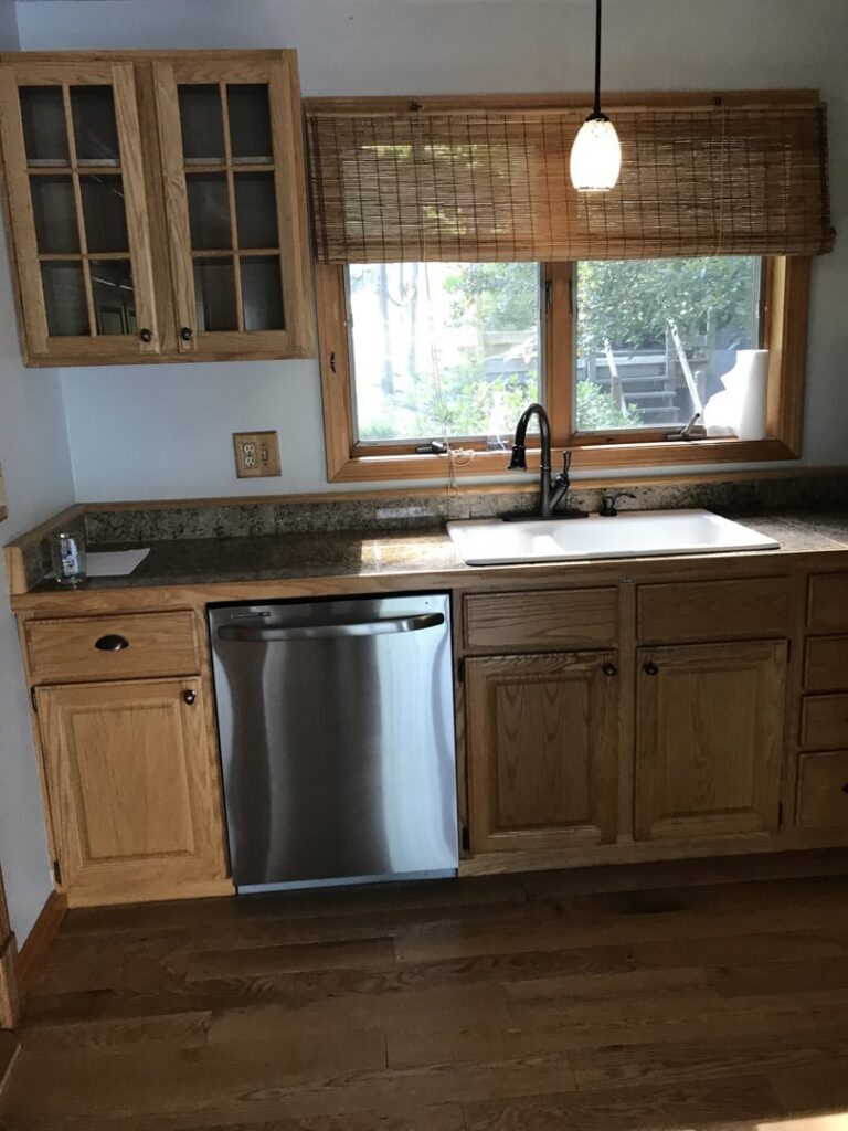 A tidy kitchen with wooden cabinets, a stainless steel dishwasher, and a clean sink, reflecting Bloom in Clean's house cleaning in Bangor, ME.