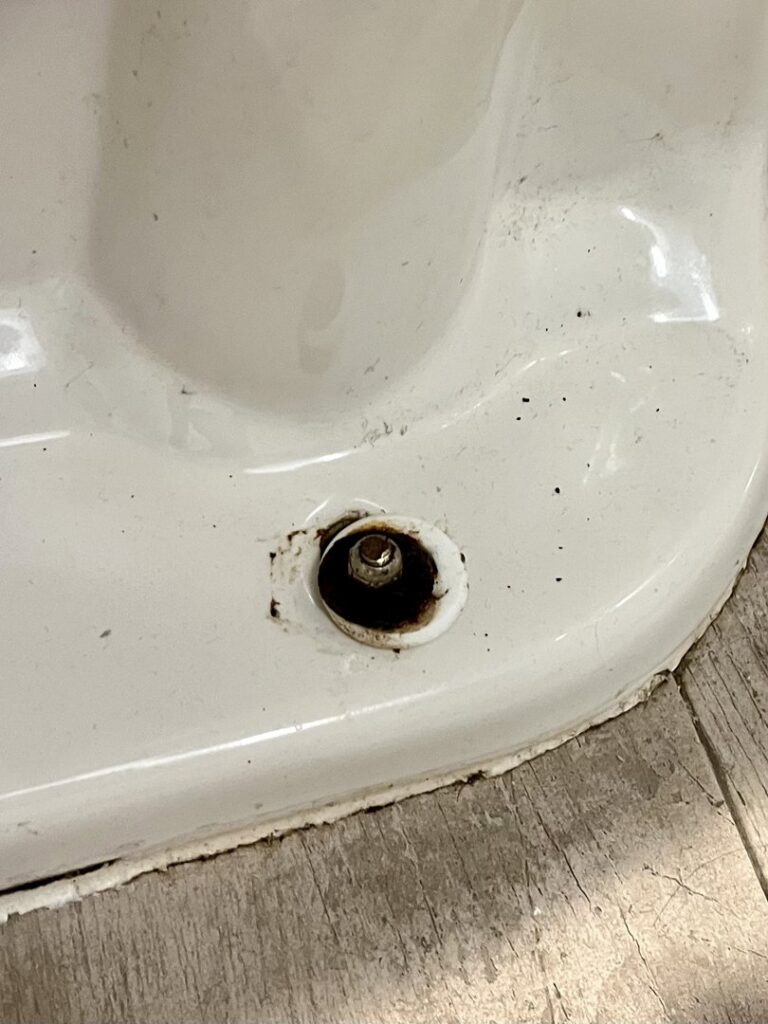 A close-up of a toilet base showing rust and water stains around the bolt, indicating a leak or water damage that Ciocca Cleaning & Restoration in Fort Wayne, IN can repair.