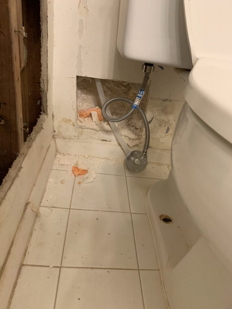 Water damage visible on the floor and exposed wall behind a toilet, indicating a leak repair by Hull Plumbing, Inc. in Oklahoma City, OK.