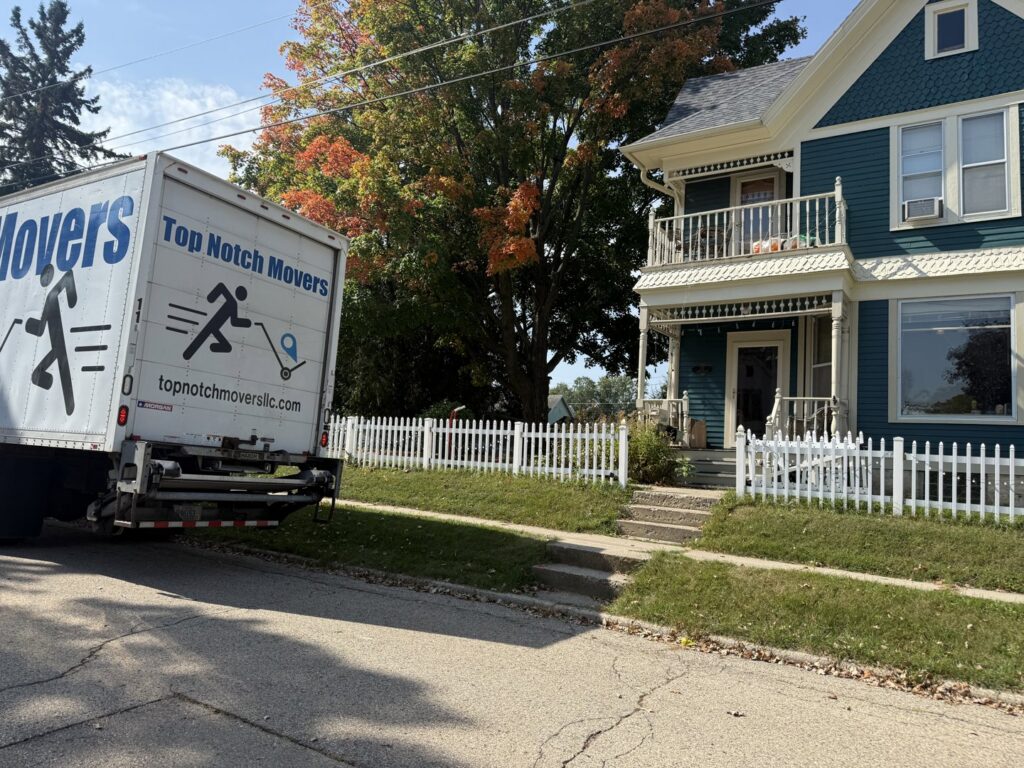 A Top Notch Movers truck parked in front of a residential house with a white picket fence in Madison, WI.