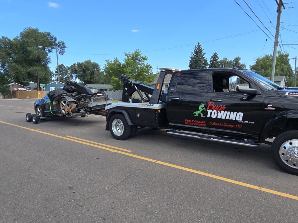 A tow truck from Towing Colorado performing accident recovery for a severely damaged black car in Colorado Springs, CO.