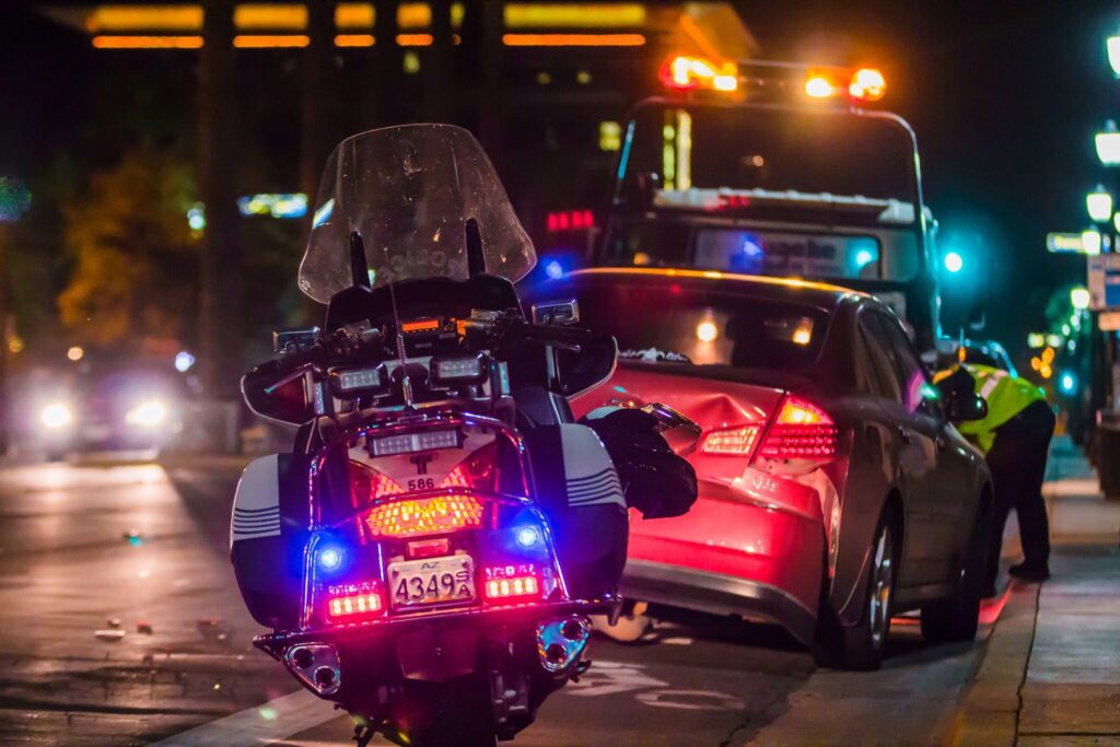 A tow truck with flashing lights at an accident scene, preparing to tow a damaged car for Elgin Towing & Recovery in Elgin, IL.