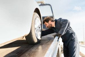 A tow truck driver inspecting a white car loaded onto a flatbed tow truck for Rochester Towing in Rochester, MN.