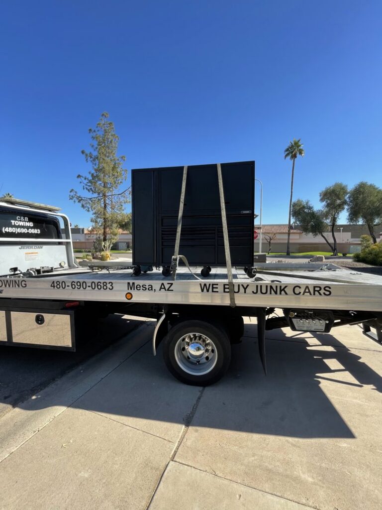 A C&B Towing flatbed truck hauling a large black toolbox or cabinet on a sunny day in Mesa, AZ.