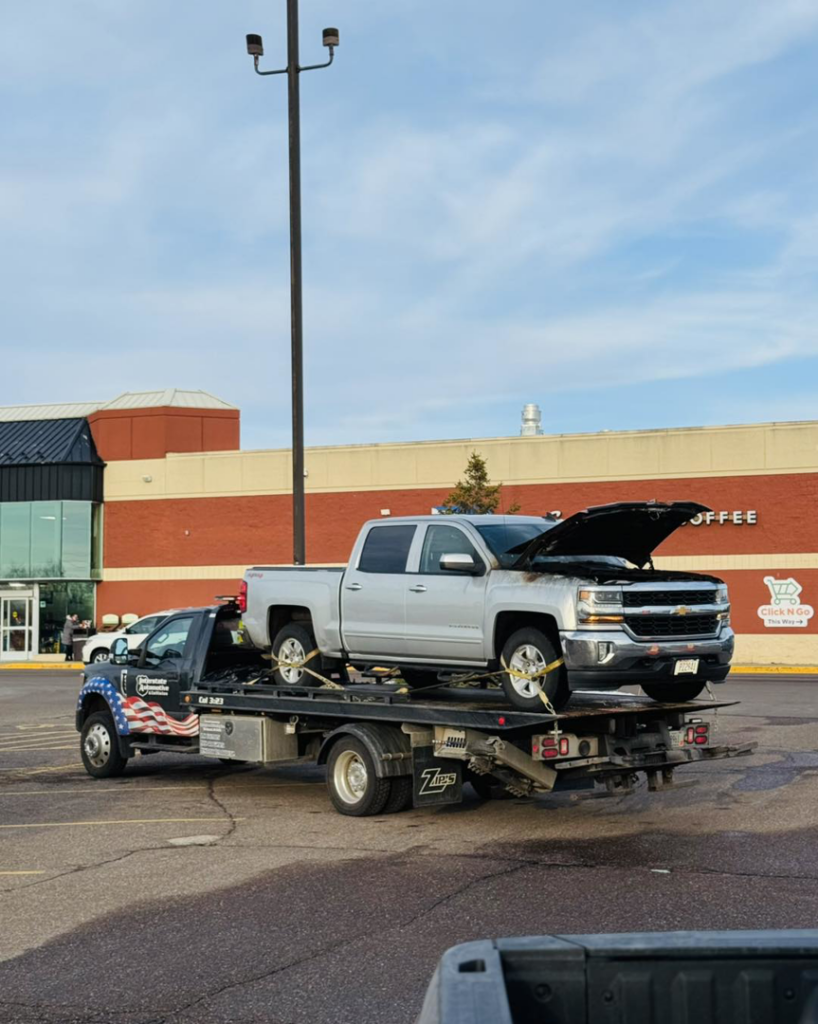 A tow truck from Interstate Automotive & Collision Center hauling a silver pickup truck on its flatbed in Eau Claire, WI.