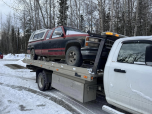 A Solid Choice Towing flatbed truck hauling a pickup truck in a snowy landscape, offering towing services in Wasilla, AK.