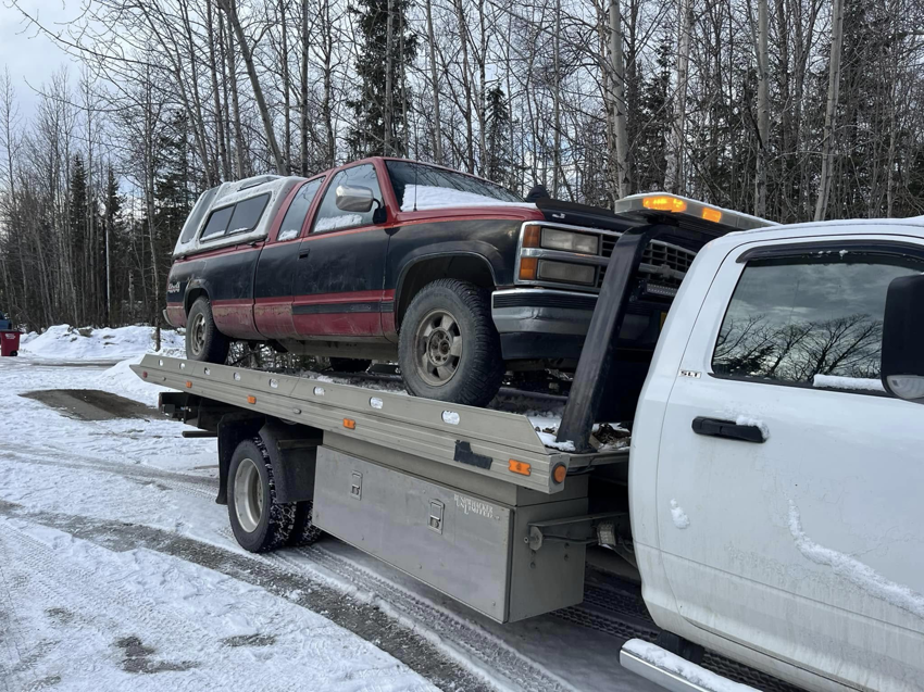 A Solid Choice Towing flatbed truck hauling a pickup truck in a snowy landscape, offering towing services in Wasilla, AK.