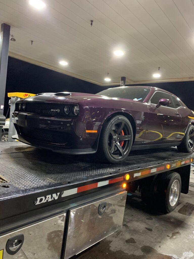A C&B Towing flatbed truck hauling a purple Dodge Challenger at a gas station in Mesa, AZ.