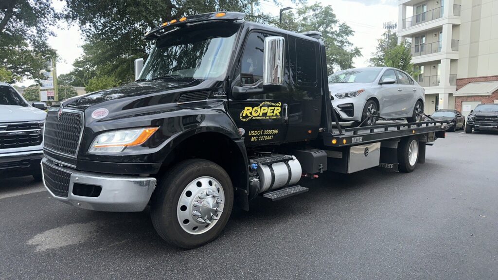 A Roper Automotive and Towing LLC flatbed tow truck hauling a silver sedan in Greenville, SC.