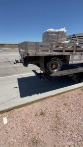 A C&B Towing flatbed truck hauling a utility trailer with wrapped cargo on a sunny day in Mesa, AZ.