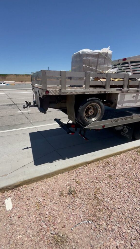 A C&B Towing flatbed truck hauling a utility trailer with wrapped cargo on a sunny day in Mesa, AZ.