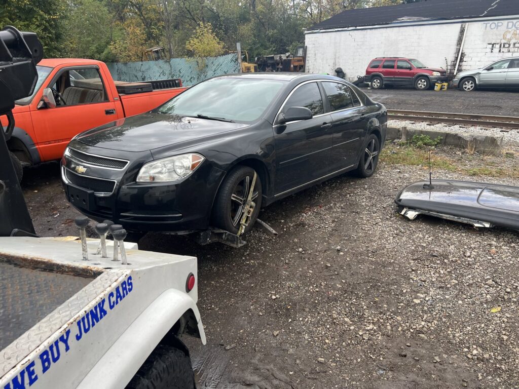 A tow truck from ALDM Management hooked to the front of a black Chevrolet Malibu in a lot in Cleveland, OH.