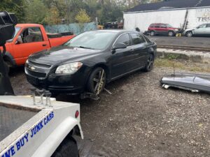 A tow truck from ALDM Management hooked to the front of a black Chevrolet Malibu in a lot in Cleveland, OH.