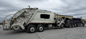 A Bevis Towing heavy-duty tow truck hooked up to a large garbage truck for towing services in Cincinnati, OH.