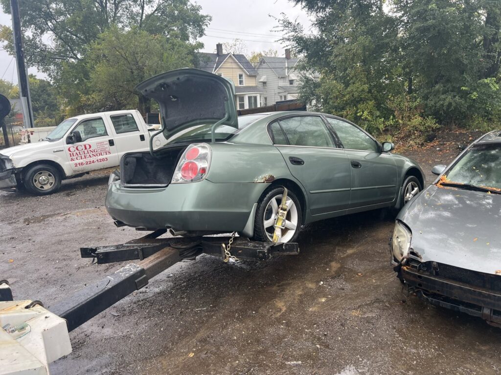 A tow truck from ALDM Management hooked to the rear of a green Nissan Altima in a lot in Cleveland, OH.