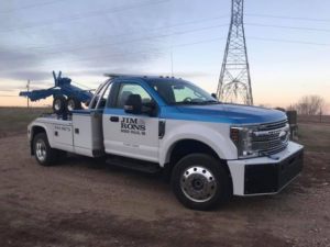 A white and blue tow truck from Jim & Ron's Service Inc. parked on a dirt road in Sioux Falls, SD.