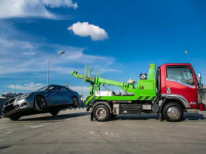 A red and green tow truck lifting a grey sedan with its boom by Safelane Towing Services Co. in Layton, UT.