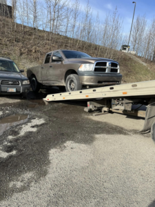 A Solid Choice Towing flatbed truck loading a brown pickup truck from the roadside, providing service in Wasilla, AK.