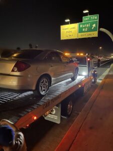 A C&B Towing flatbed truck loading a silver sedan on a highway at night in Mesa, AZ.