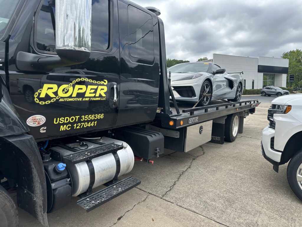 A Roper Automotive and Towing LLC flatbed tow truck loading a white sports car in Greenville, SC.